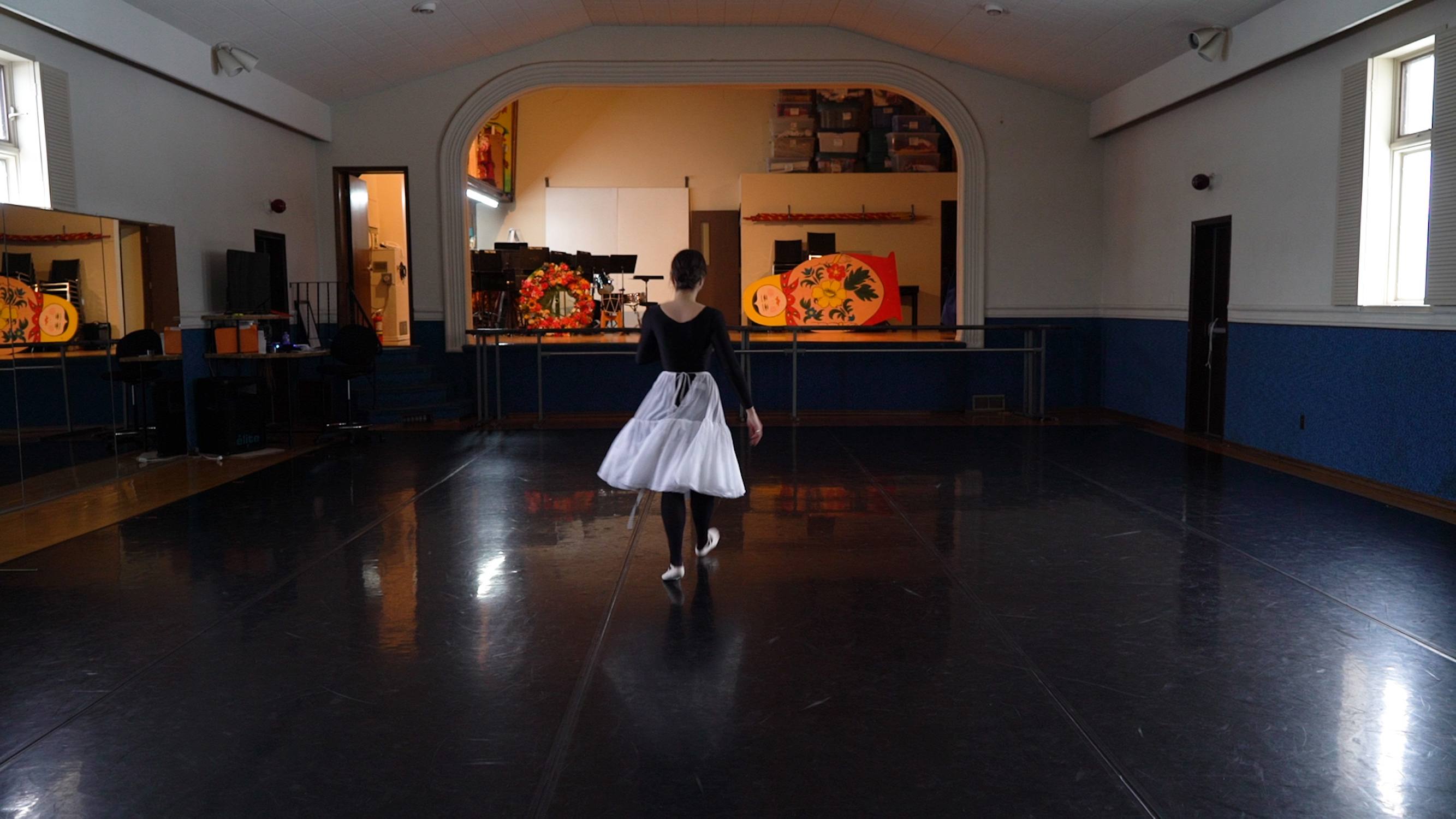 A woman wearing a wreath made of thin beeswax candles is lit. She stares directly into the camera. Hanging from the wreath are severed braids.
